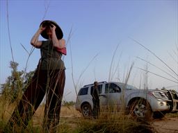 woman sighting in bush in front of 4x4 in West Africa